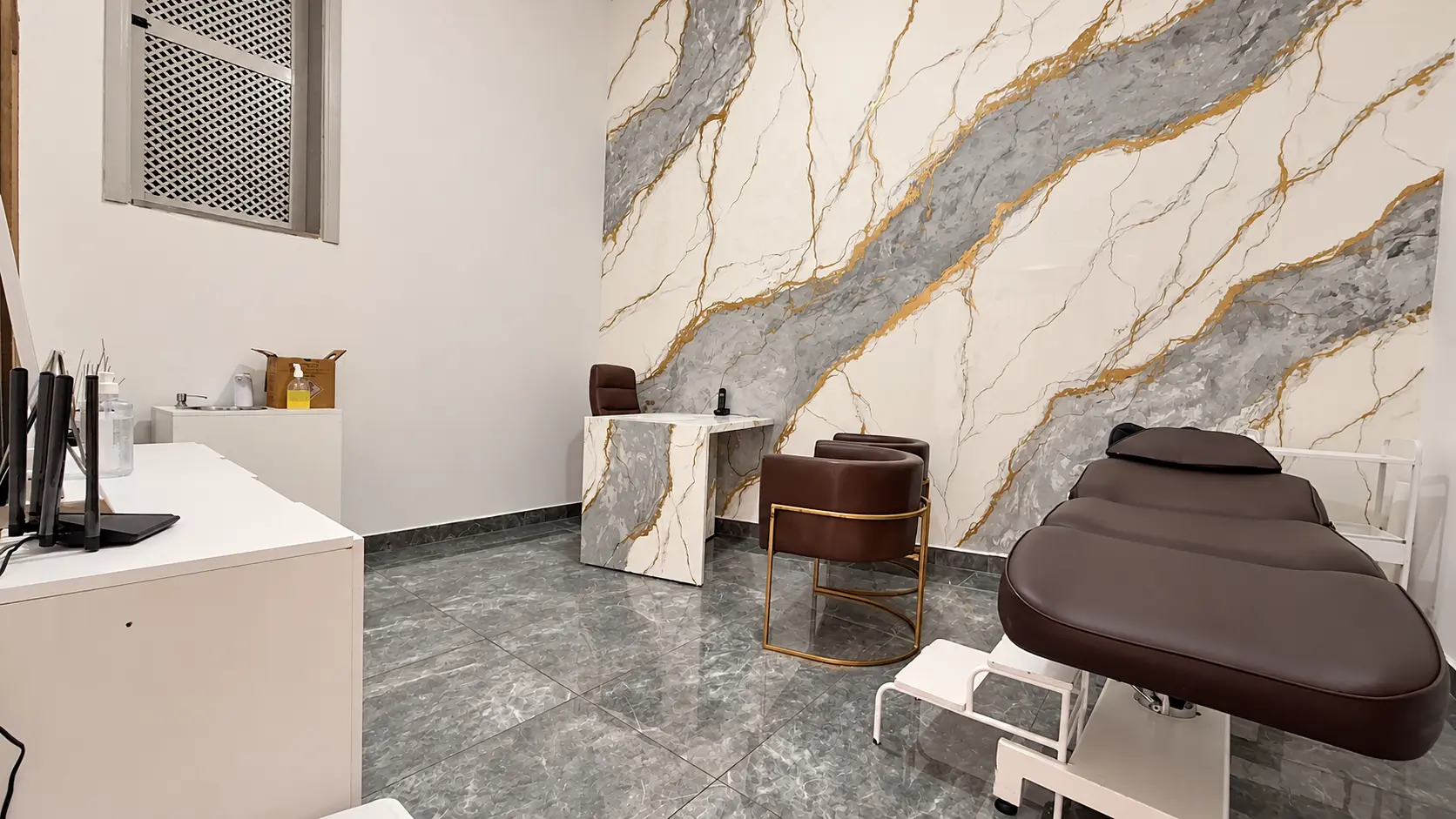 Consultório de avaliação com painel marmorizado, poltronas marrons e maca