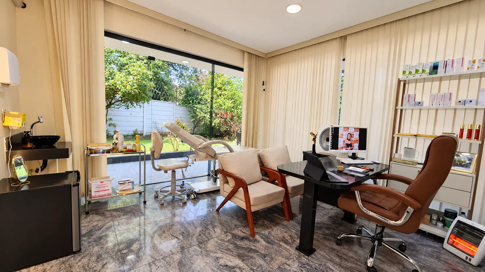 Sala de estética facial com mesa de atendimento, poltronas beges e maca, com vista para o jardim