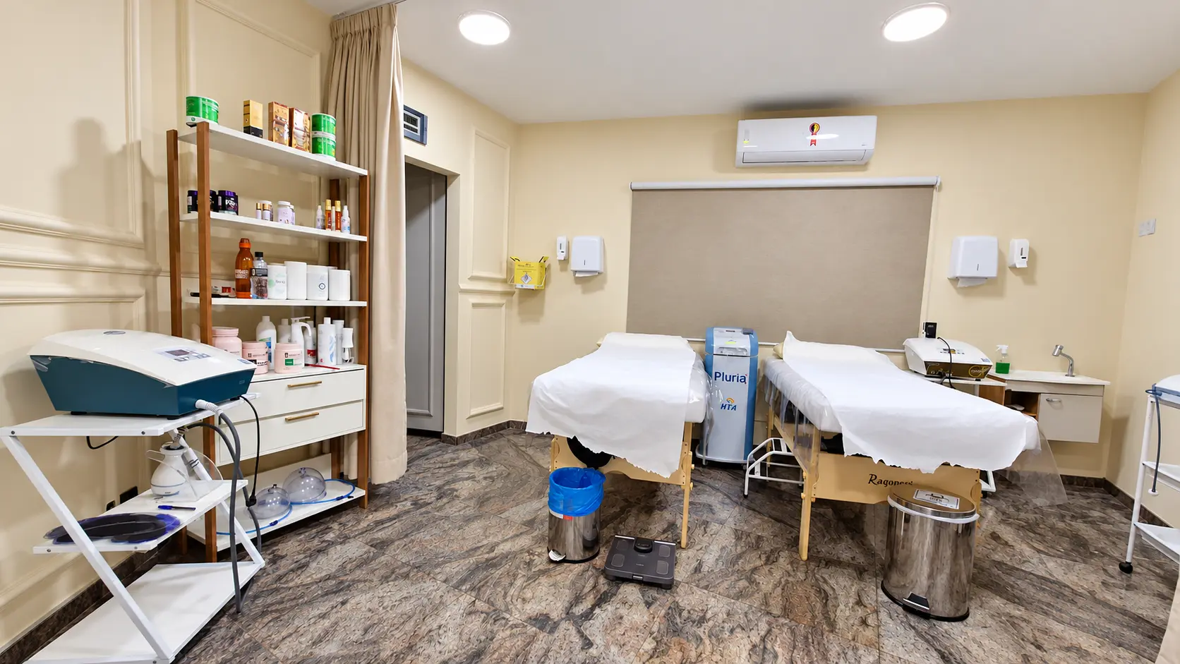 Sala de estética corporal com duas macas, equipamento estético e estante de cosméticos